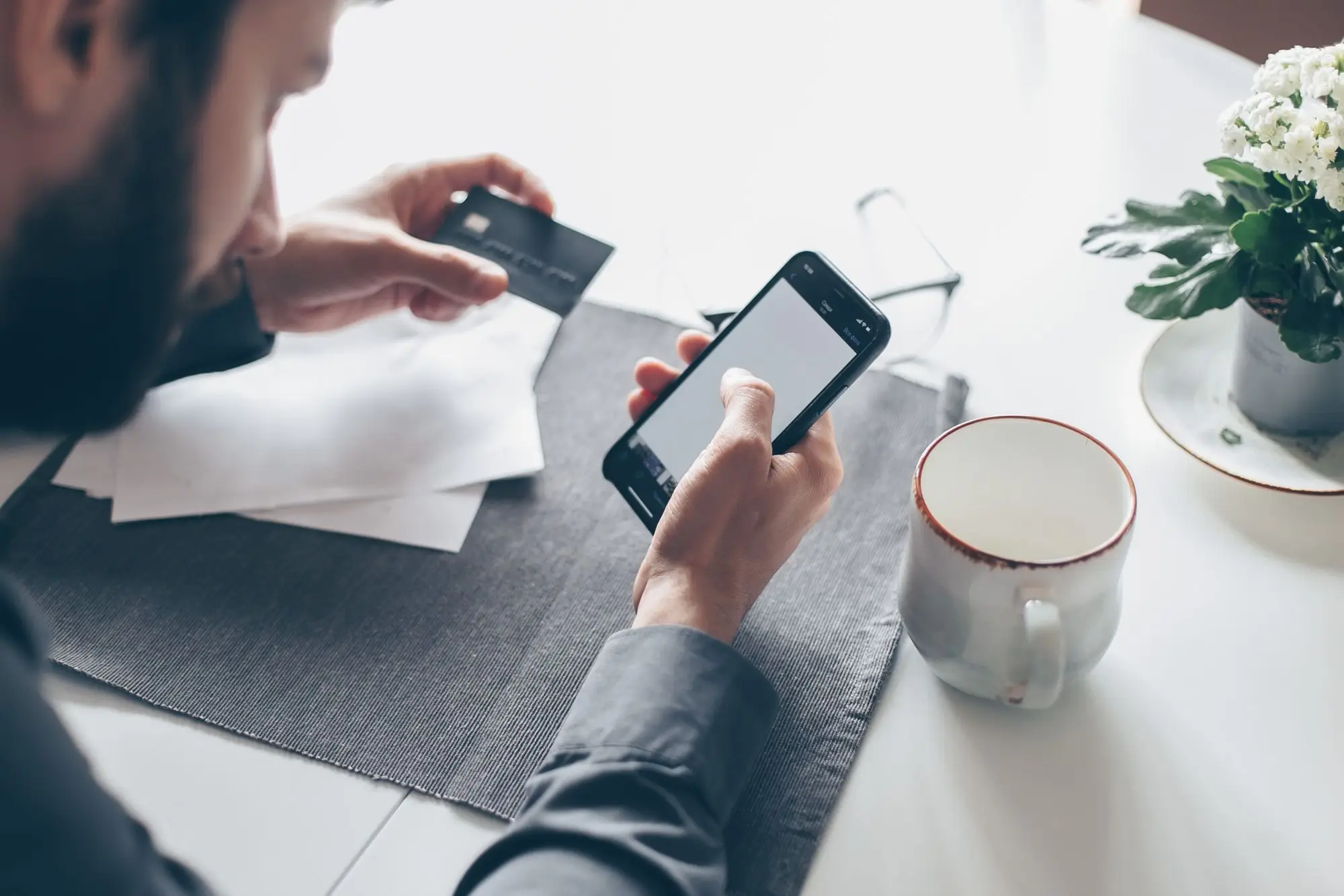 Business owner checking a bank transfer on his phone, with invoices and a card on the desk
